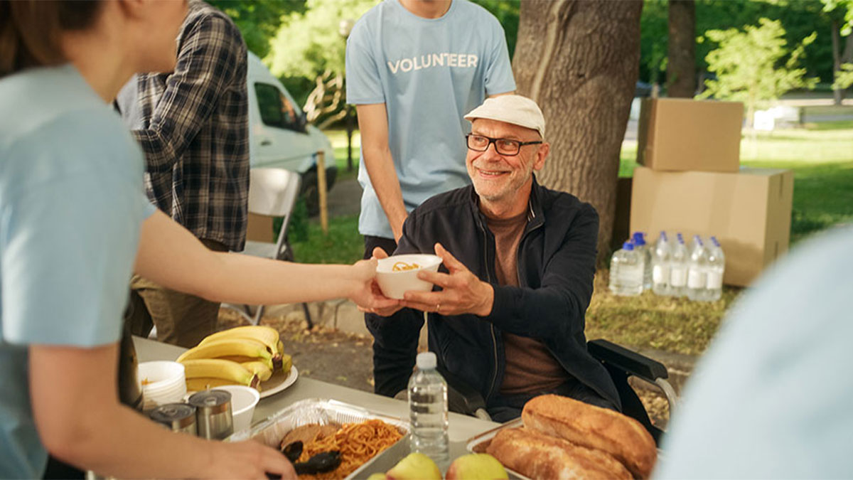 Man in a wheelchair accepting food from a volunteer during a food drive at a park